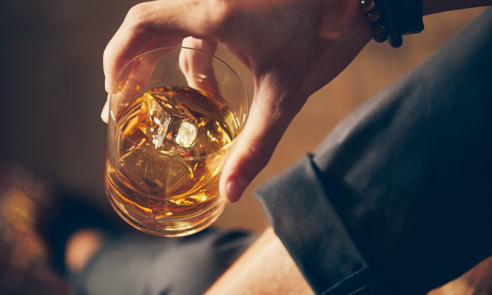 high angle closeup shot of a male holding a glass of whiskey